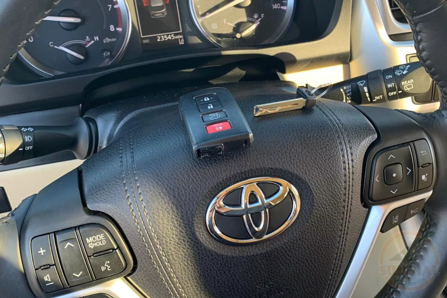 Driver's perspective of a Toyota steering wheel with multifunction controls and a visible key fob with a dashboard in the background.