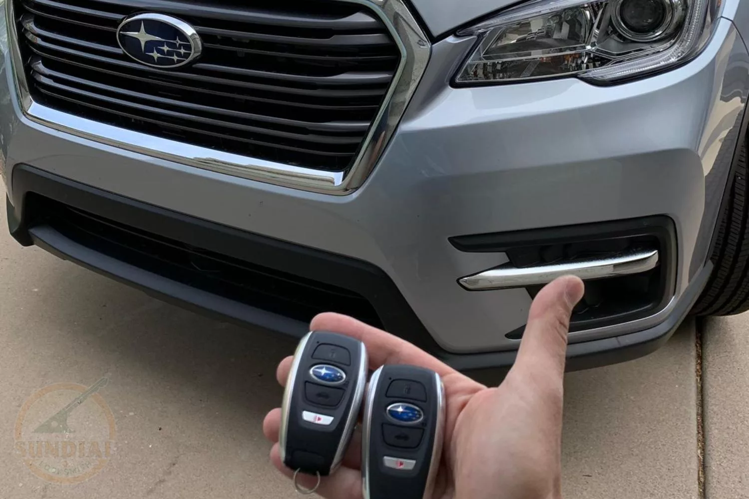 Hand holding Subaru car keys in front of vehicle