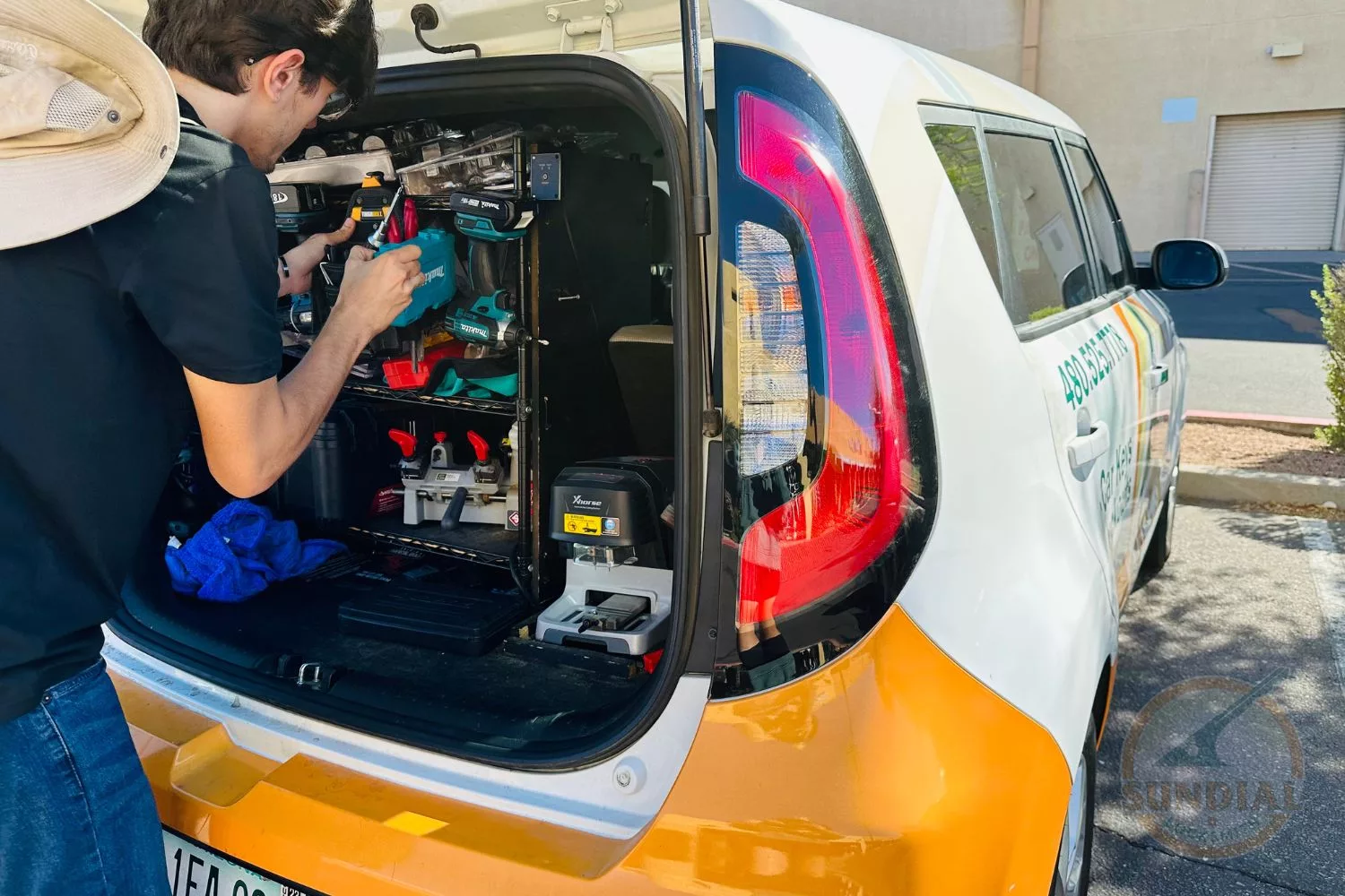 A locksmith works from the back of a service van equipped with various tools and key cutting machines