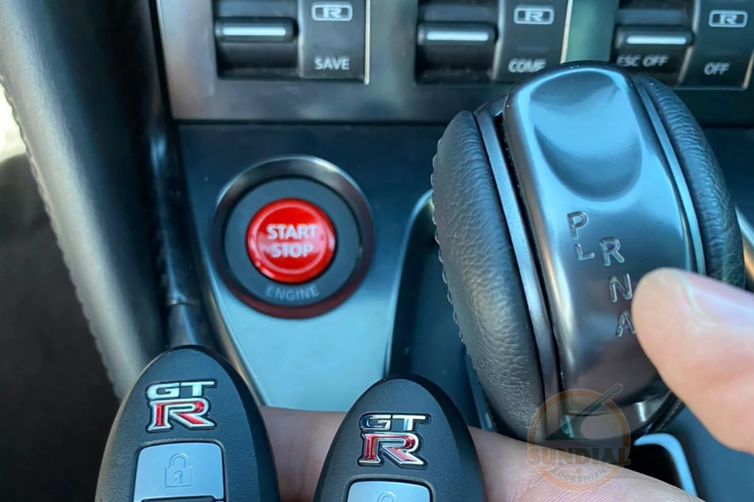 A hand holding two key fobs with the GT-R logo in front of the Nissan GT-R's start button and gear selector