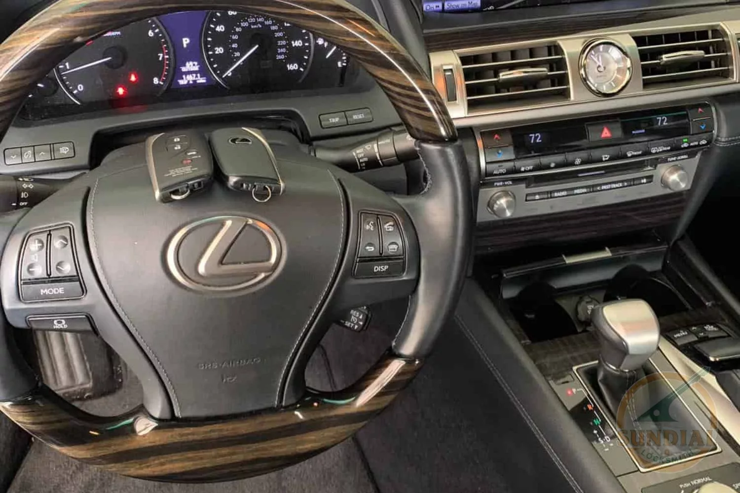 A pair of Lexus car keys resting on the steering wheel with the vehicle's dashboard illuminated