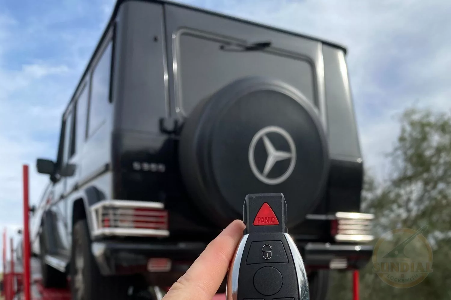 Hand holding Mercedes-Benz car key fob with vehicle behind.