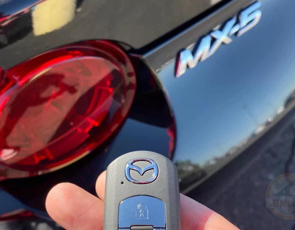 Close-up of a hand holding a new Mazda key fob with the MX-5 model emblem in the background.