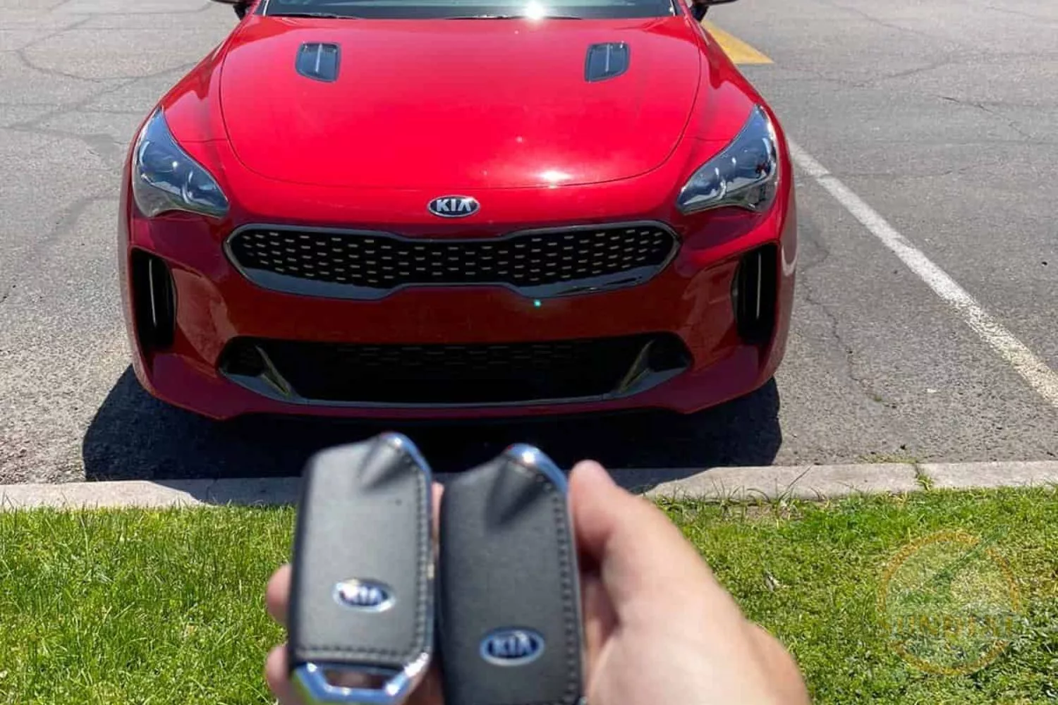 A hand holding two Kia car keys with a red Kia vehicle in the background.