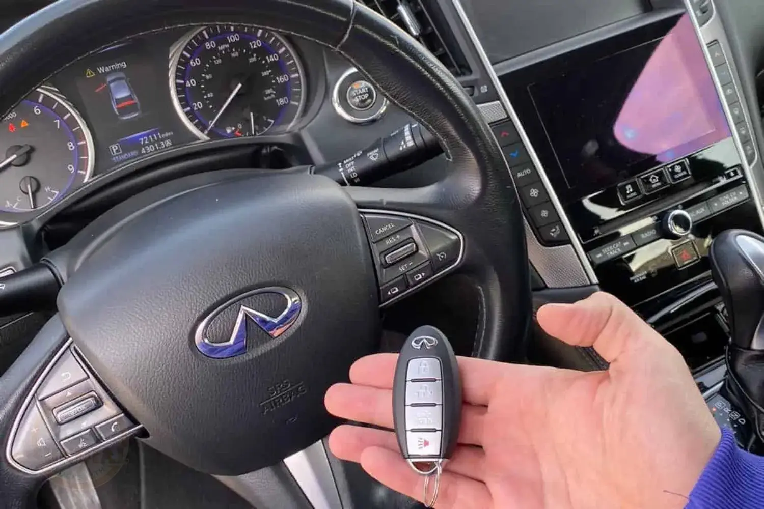 A person's hand holding a keyless entry fob in front of a vehicle's steering wheel with the start/stop button and dashboard visible
