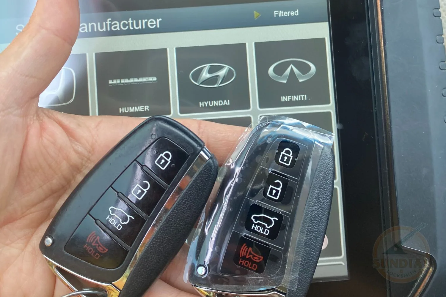 Two car key fobs, one with visible wear and the other with a protective plastic cover, held in front of a car manufacturer selection screen displaying logos for Hummer, Hyundai, and Infiniti.