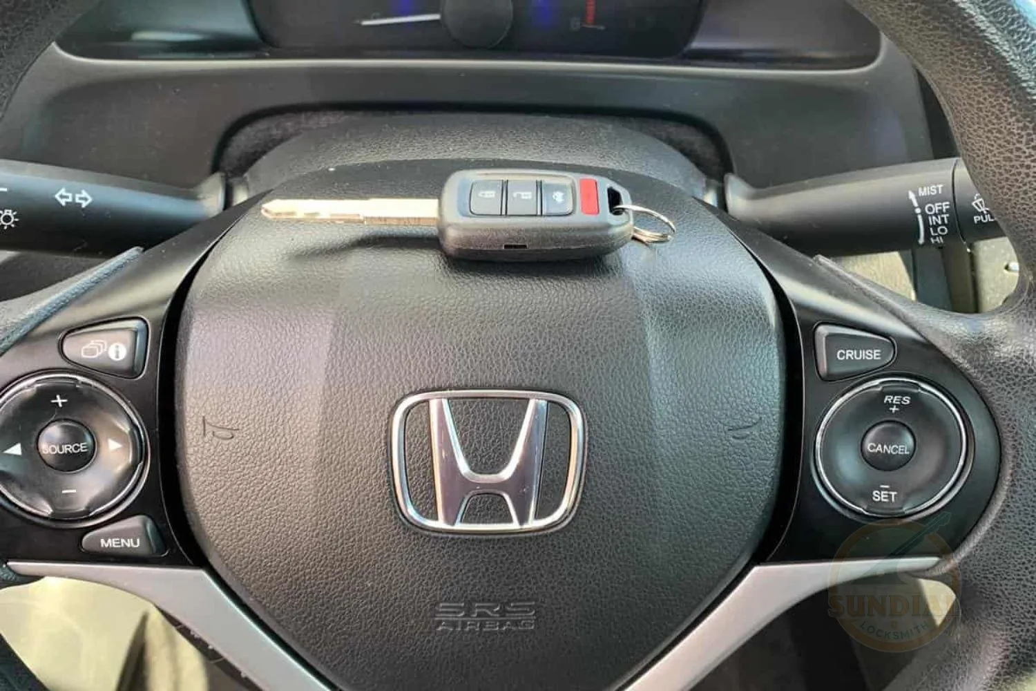 A Honda car key fob resting on the center of a Honda steering wheel with control buttons.