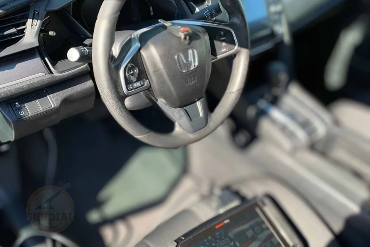 A blurred image focused on the Honda logo on a steering wheel, with the car's dashboard and center console softly out of focus in the background
