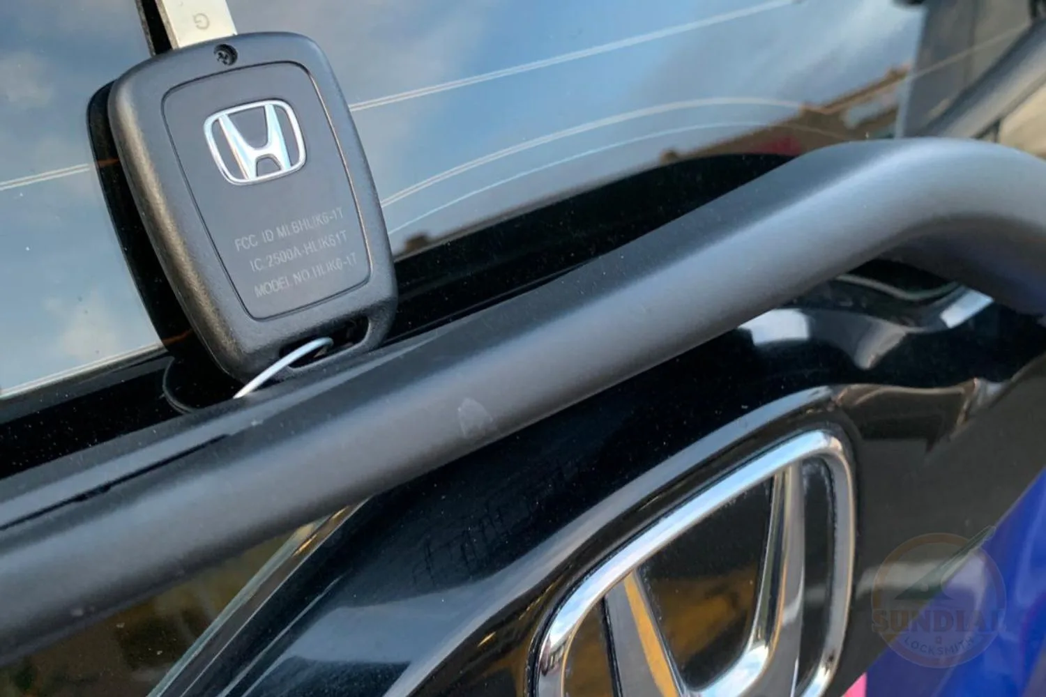 A close-up image of a black Honda key fob with the Honda logo, attached to a key, resting on a car's chrome handle.
