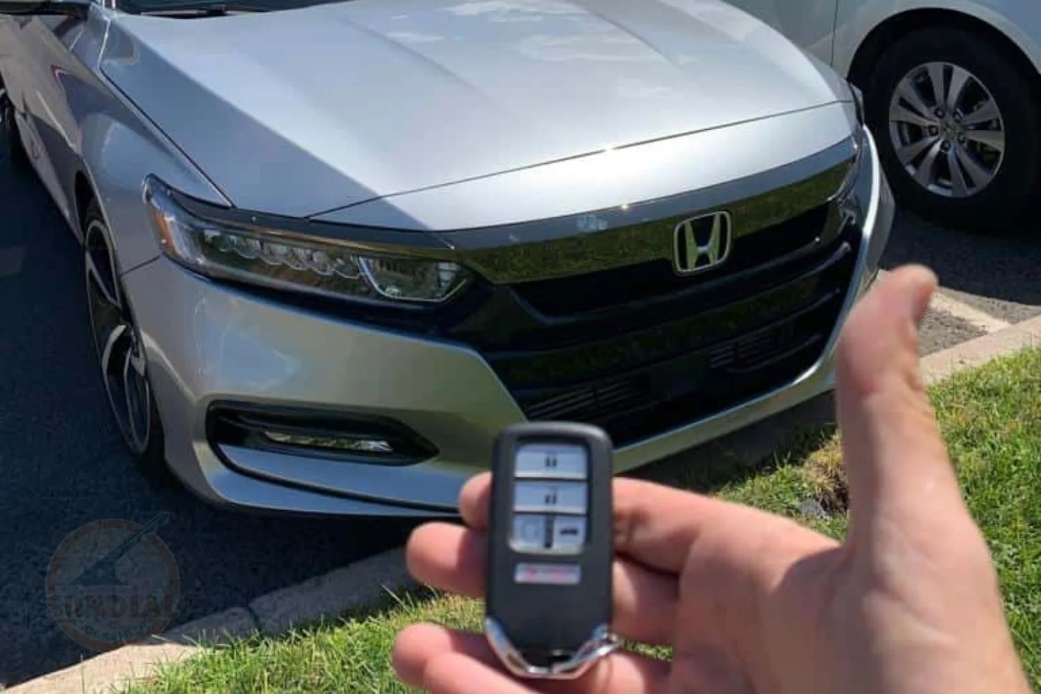A focused view of a Honda key fob held up with a silver Honda car blurred in the background.