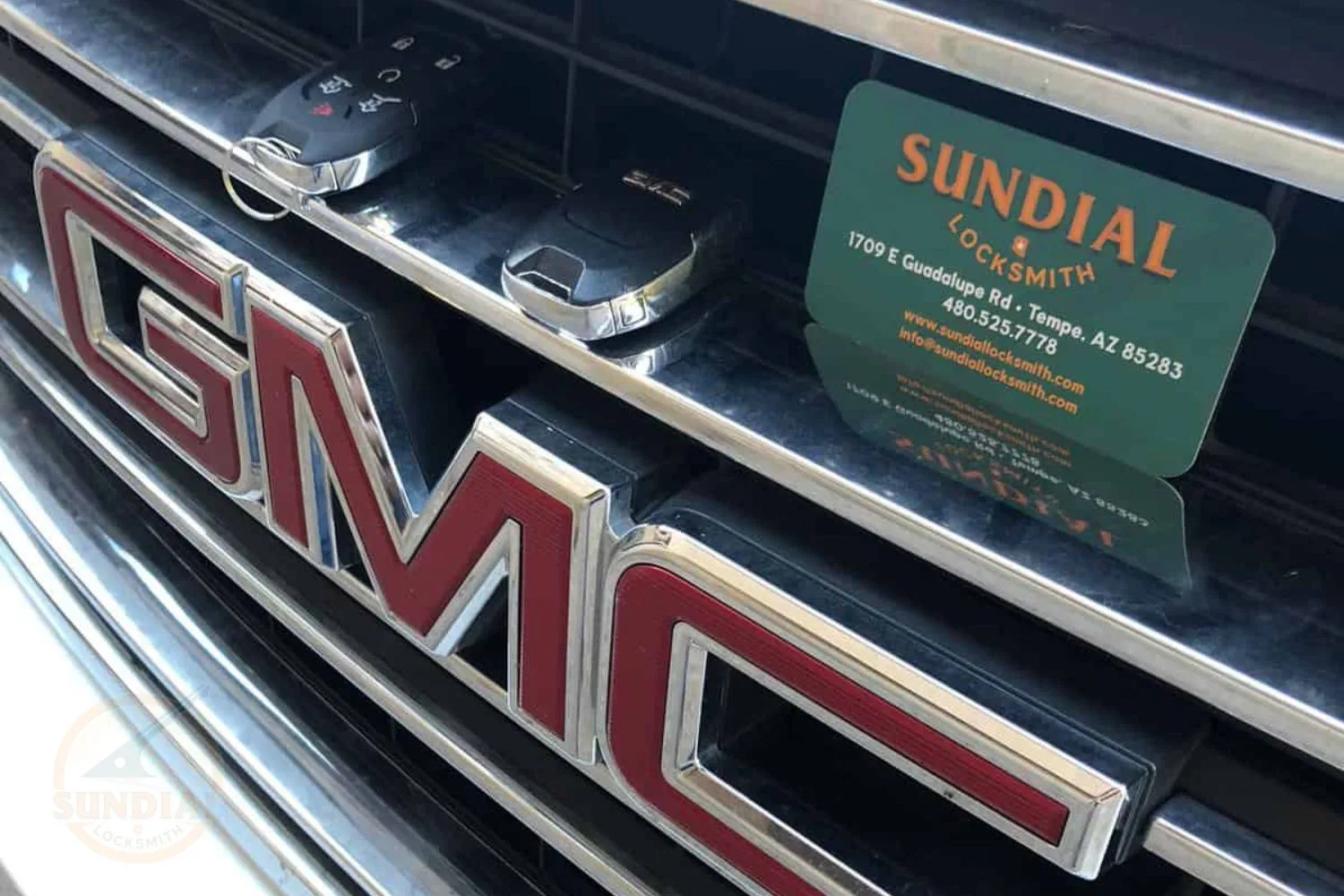 Two car key fobs and a Sundial Locksmith business card placed on the chrome grille of a vehicle with the GMC logo