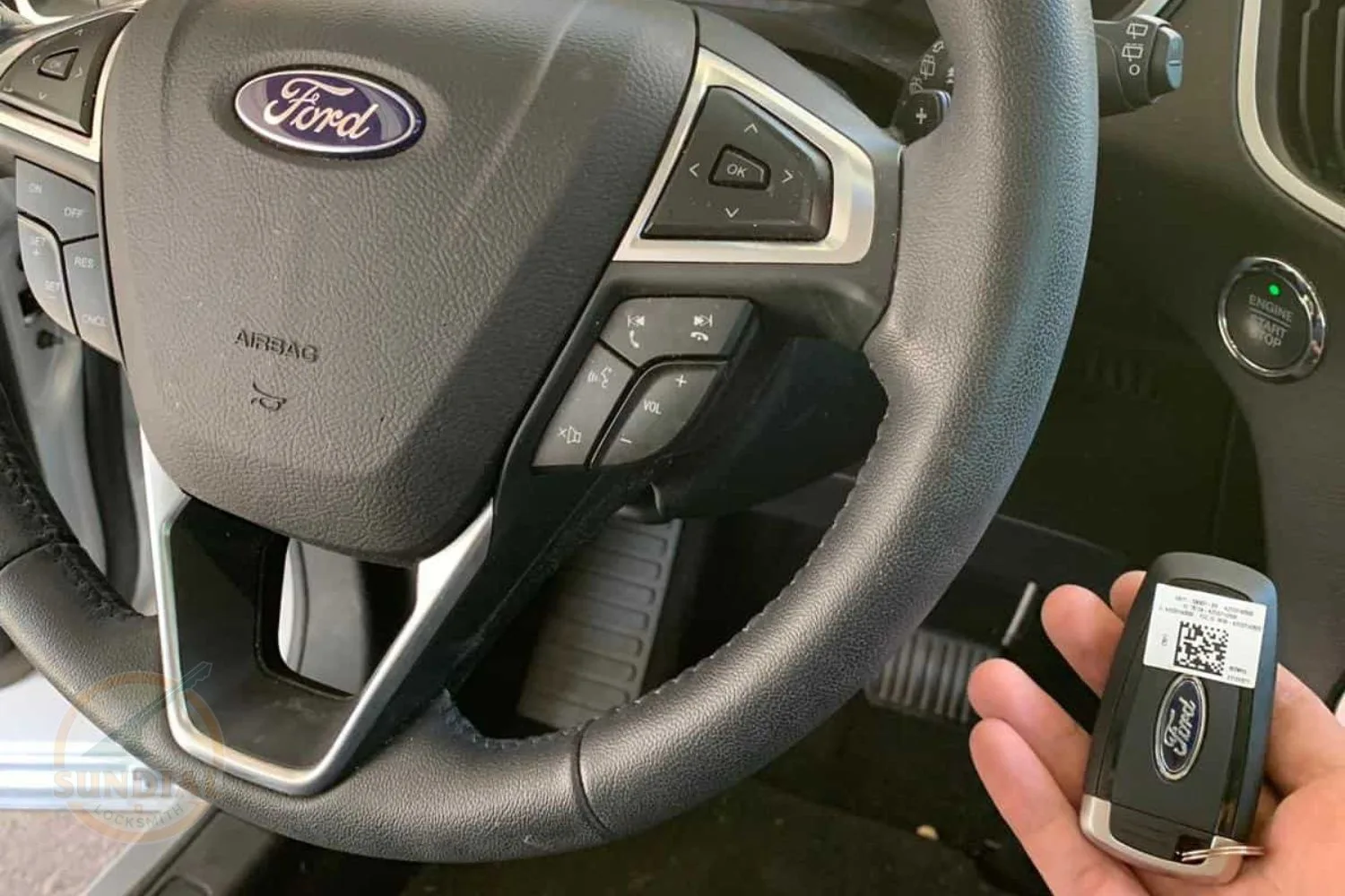 A hand holding a Ford car key fob with a QR code in front of a Ford vehicle's steering wheel with mounted controls.