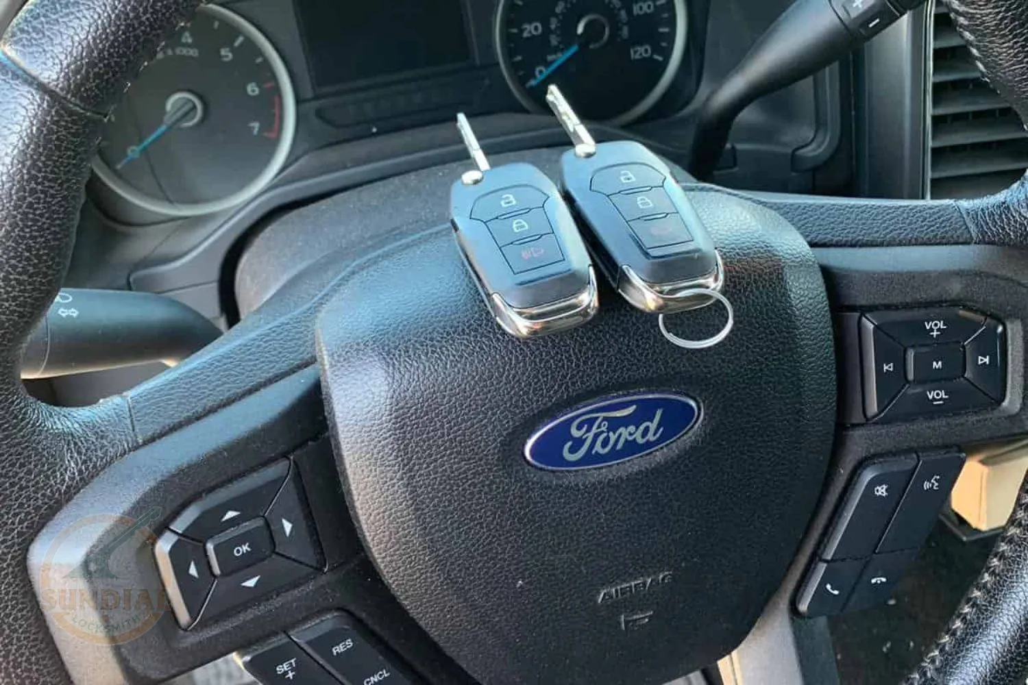 Two Ford car keys placed on a Ford vehicle's steering wheel with the brand logo and control buttons.