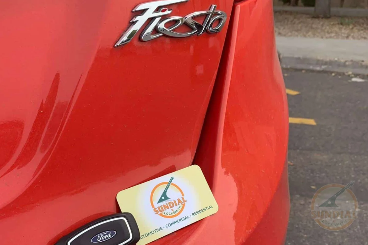 A Ford car key fob and a Sundial Locksmith business card displayed on the rear of a red Ford Fiesta.