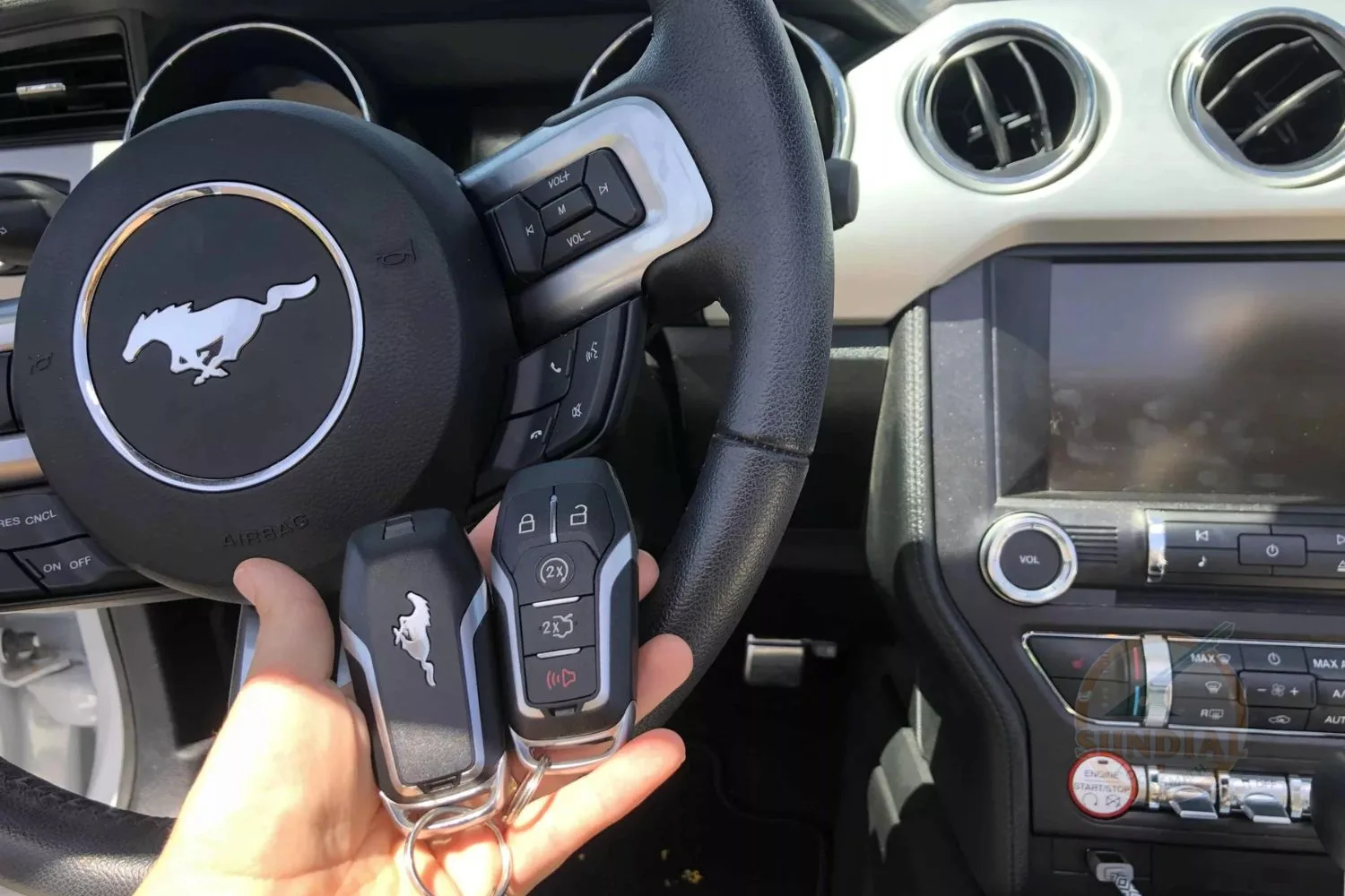 A pair of Ford Mustang key fobs held in front of the steering wheel with the Mustang logo, inside the car's interior.