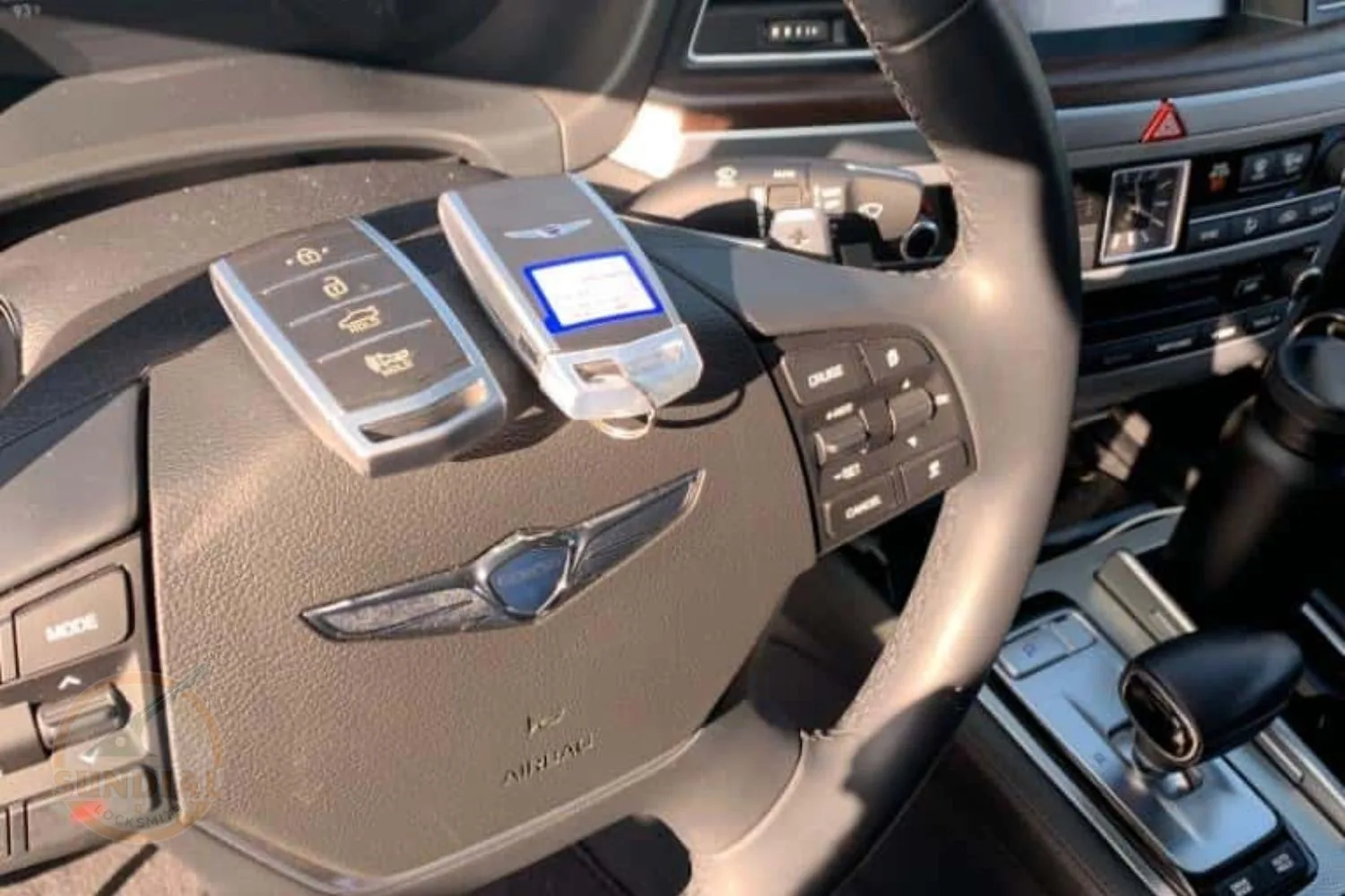 Two modern key fobs placed on top of a car's steering wheel with the car's interior controls in the background.
