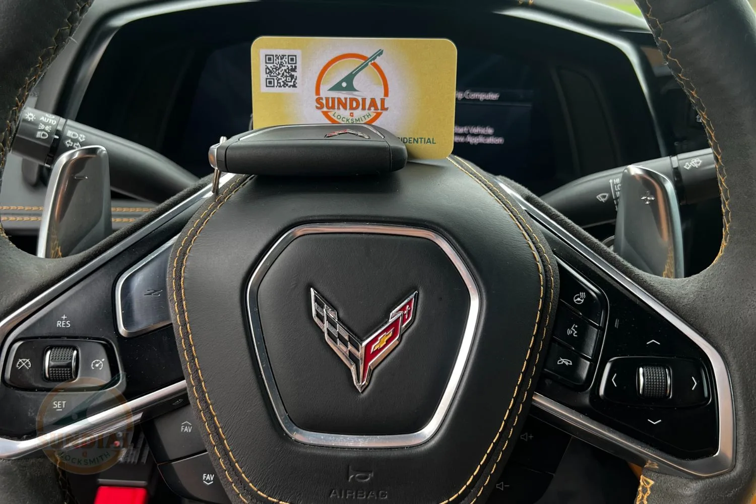 A close-up of a luxurious car's steering wheel with an embroidered emblem and a key fob placed over a business card.