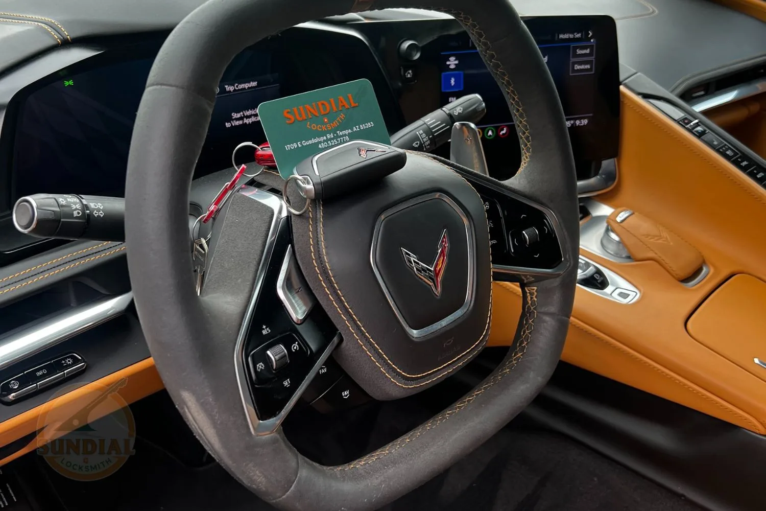 A driver's perspective of a luxury car's steering wheel with intricate stitching, a polished emblem, and a locksmith's business card.