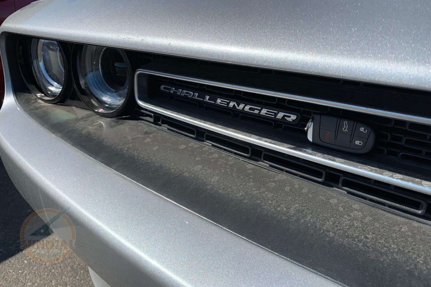 A key fob displayed in front of the grille of a Dodge Challenger with the car's name clearly visible.