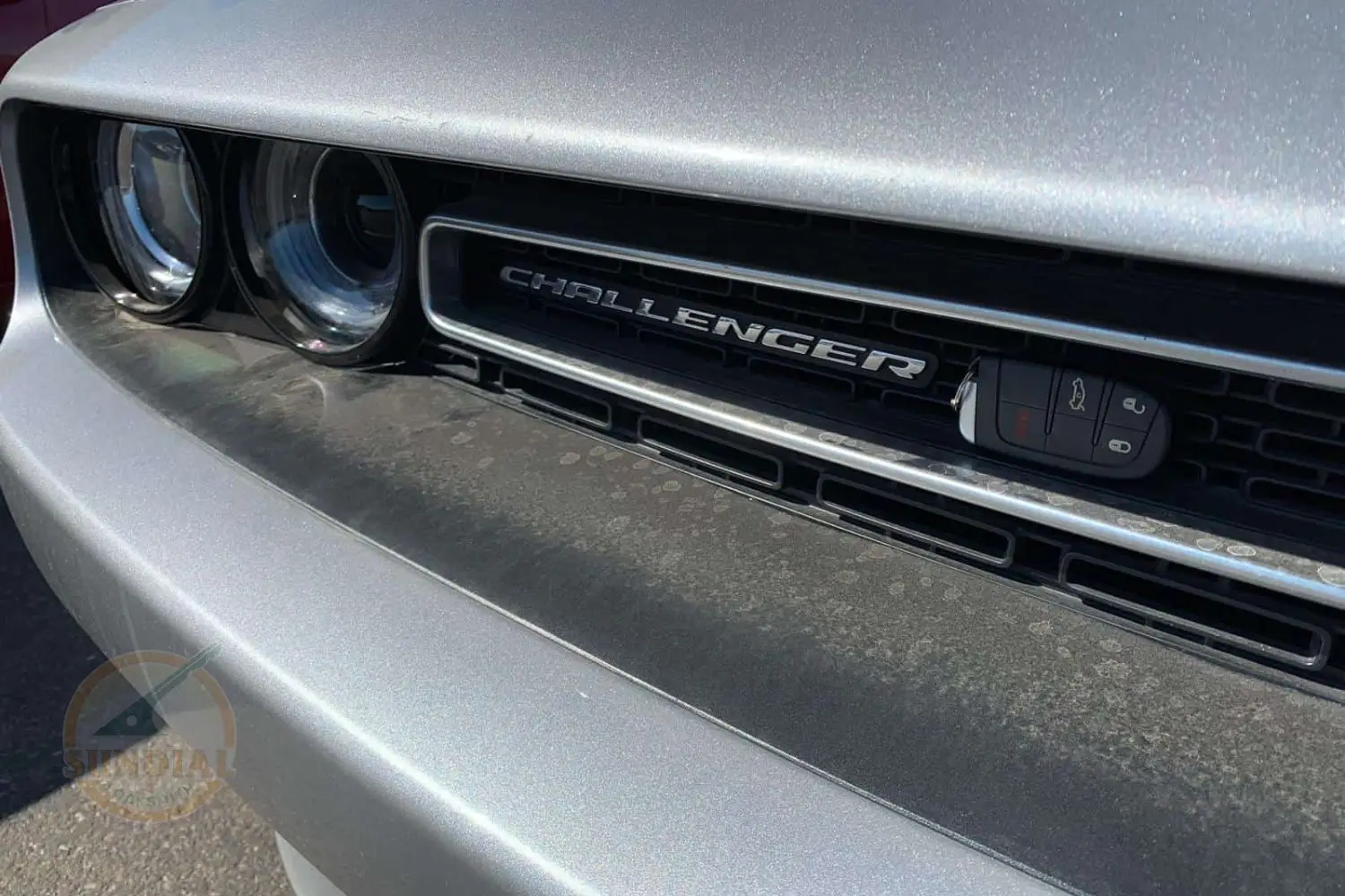 A key fob displayed in front of the grille of a Dodge Challenger with the car's name clearly visible.