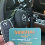 Nissan car key and Sundial Locksmith business card held in hand with car dashboard in the background.