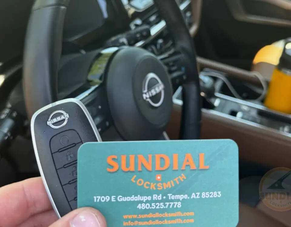 Nissan car key and Sundial Locksmith business card held in hand with car dashboard in the background.