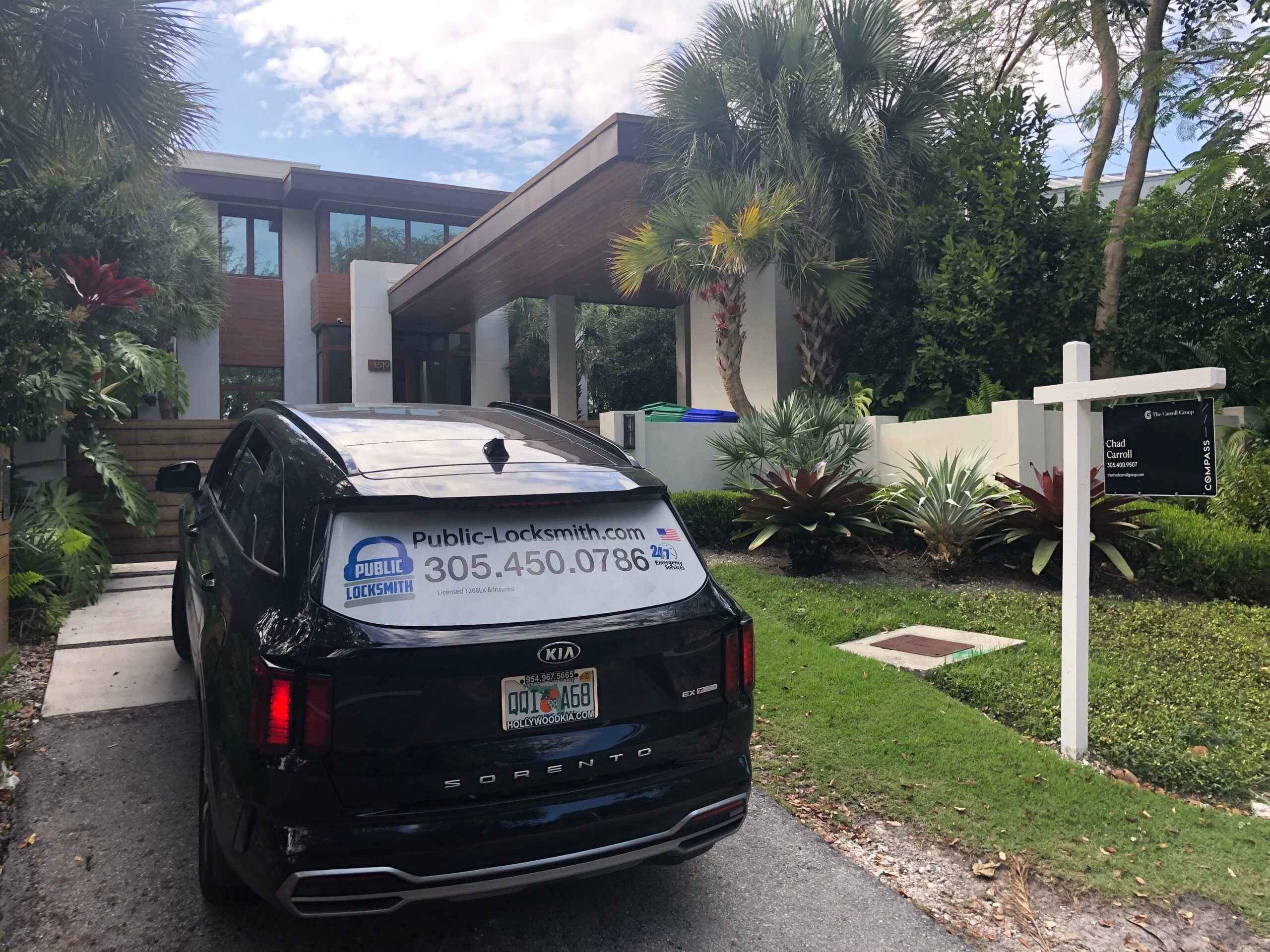 A black Sundial Locksmith SUV parked in the driveway of a modern two-story home with a real estate sign on the front lawn.