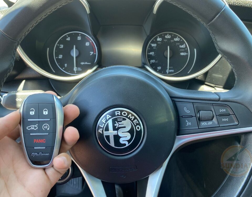 A close-up of an Alfa Romeo steering wheel with a hand holding the car's key fob in front.