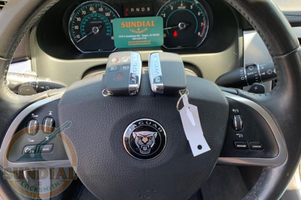 Two Jaguar smart key fobs resting on the steering wheel of a Jaguar vehicle, with a Sundial Locksmith business card visible on the dashboard.