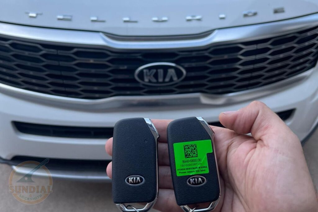 Can You Rekey a Lock to Match an Existing Key You Already Carry? A hand holding two Kia smart key fobs in front of a white Kia vehicle grille, one key displaying a green QR code programming screen.