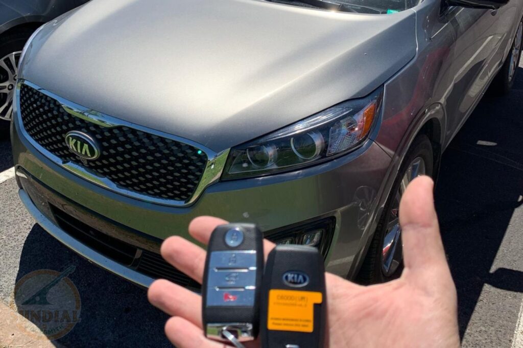 Can You Rekey a Lock to Match an Existing Key You Already Carry? A hand holding a Kia key fob in front of a silver-green Kia Sorento SUV in a parking lot.