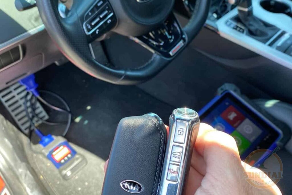 A technician holds a black car key fob next to a handheld diagnostic device inside a vehicle interior with a steering wheel visible in the background.
