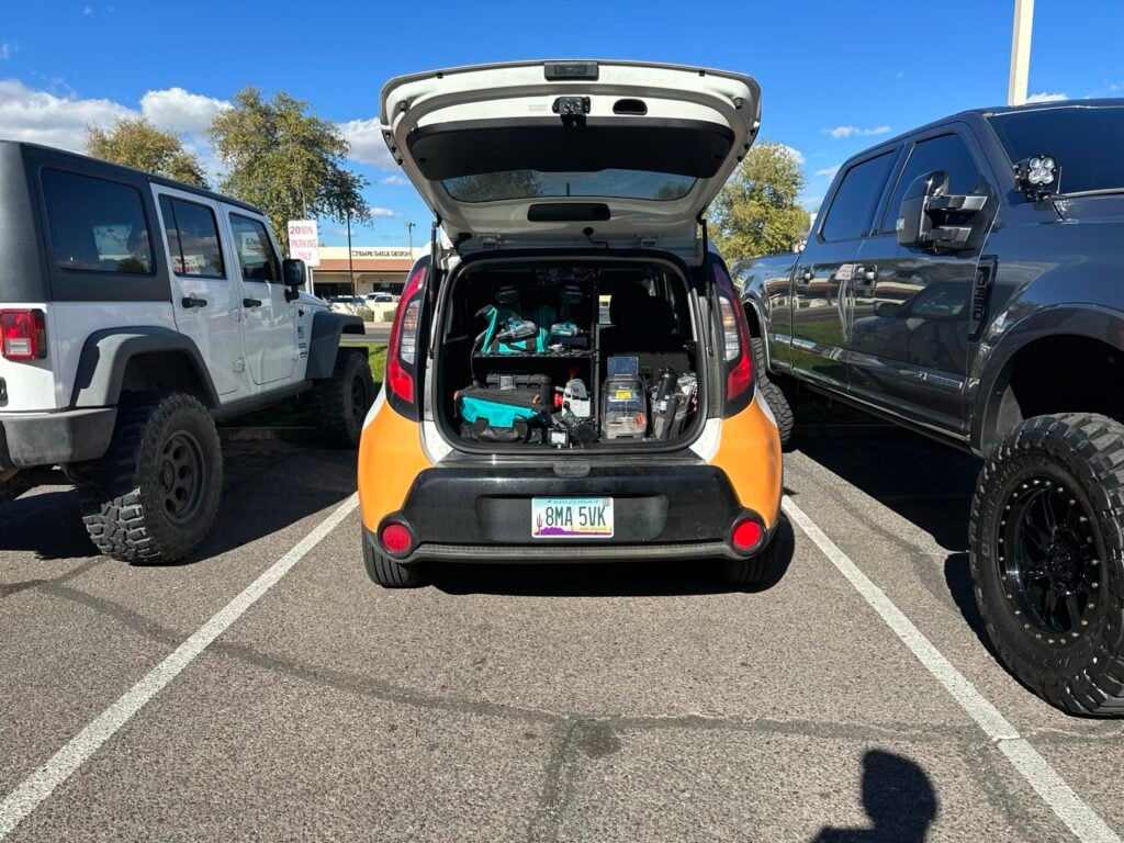 What to Expect When a Locksmith Arrives at Your Door The open hatchback trunk of a small orange and black car packed with locksmith tools, equipment, and supplies in a parking lot.