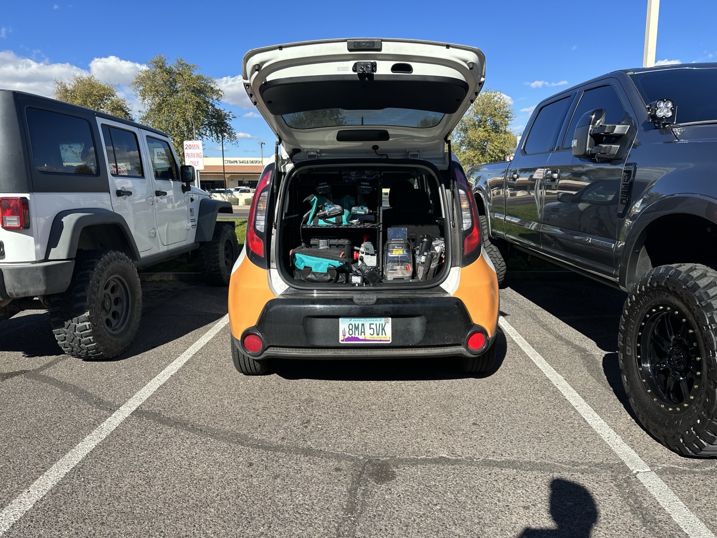 The open hatchback trunk of a small orange and black car packed with locksmith tools, equipment, and supplies in a parking lot.