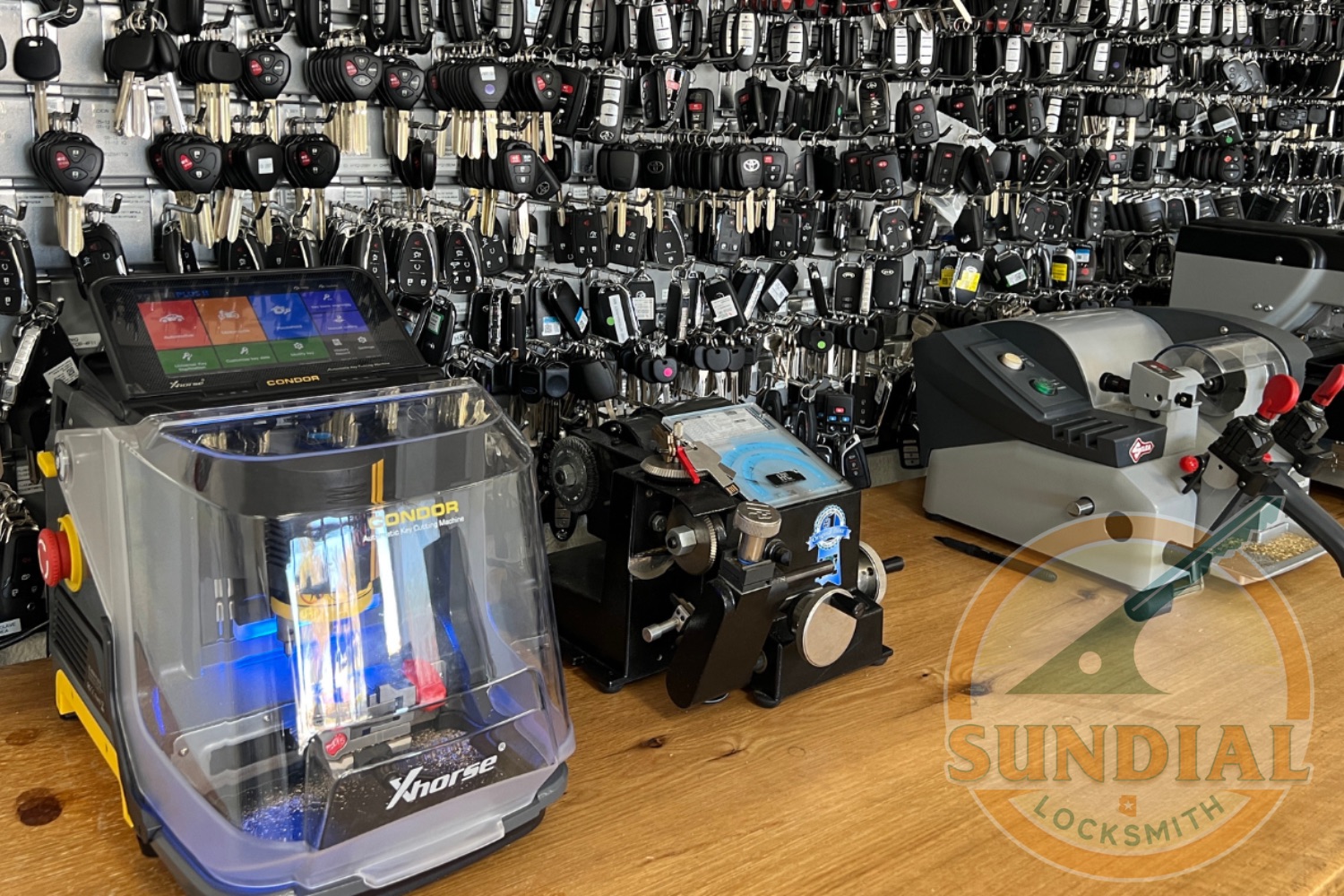 A locksmith shop workbench displaying multiple key cutting machines including an Xhorse key duplicator, surrounded by walls covered with hundreds of key blanks organized on display boards.