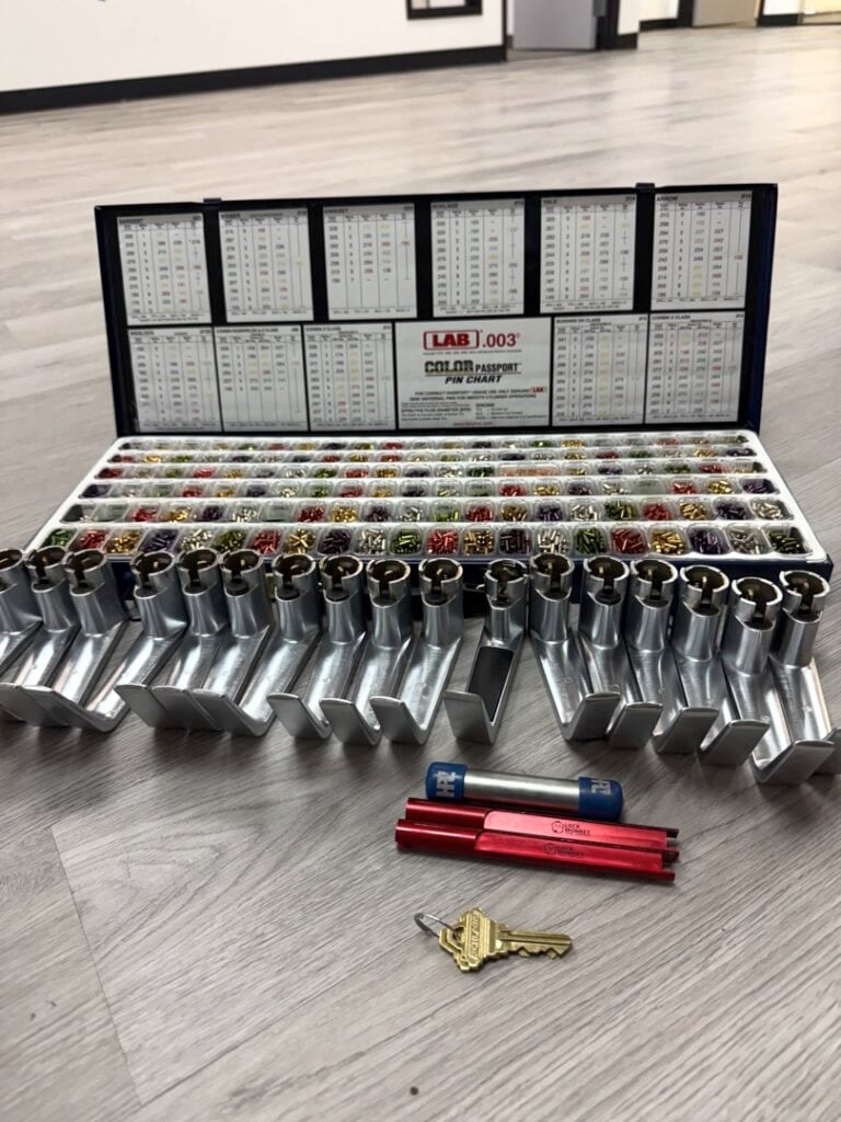 Can a Locksmith Rekey a Car's Ignition? Here's the Honest Answer A locksmith key pinning kit displayed on a wood floor, featuring rows of color-coded pin tumblers in a metal tray with a reference chart, alongside a red pinning tool and two brass keys.