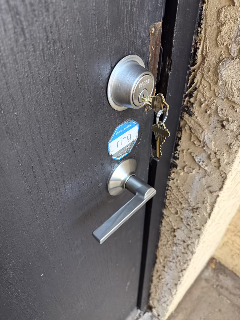 A silver deadbolt lock with a key inserted alongside a lever-style door handle mounted on a dark metal exterior door.