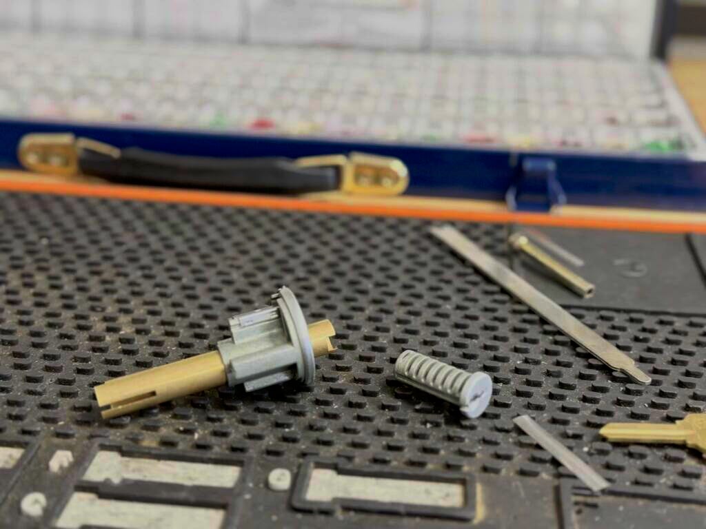 Can You Rekey Your Own Locks? What DIY Gets Right and Wrong Disassembled lock cylinder parts including a plug, pins, and small tools laid out on a textured gray work mat.