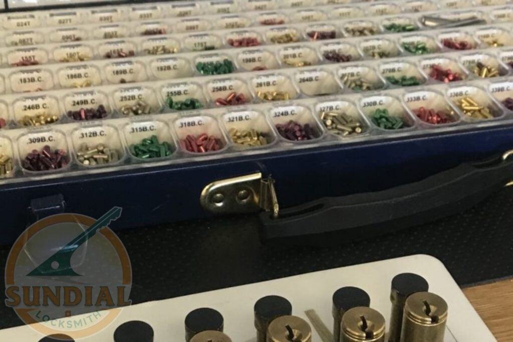 A professional locksmith's organized carrying case filled with rows of colorful assorted key pins and rekeying components, with brass lock cylinders displayed in the foreground.