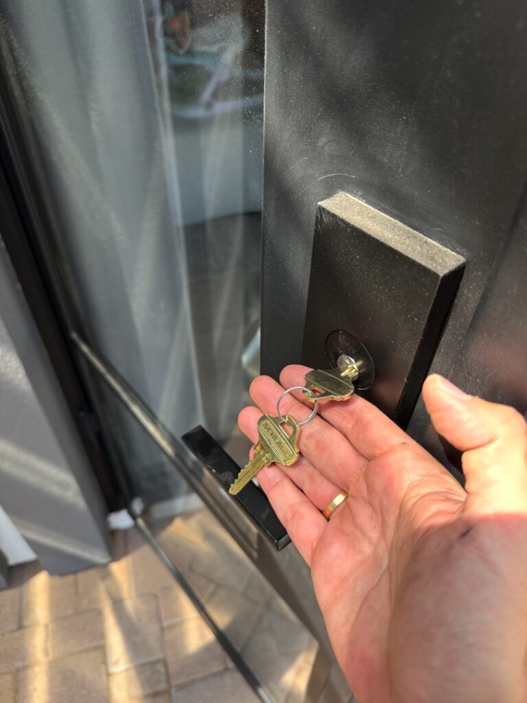 A person holds a set of brass keys in their open palm next to a black door handle and lock on a modern entry door.
