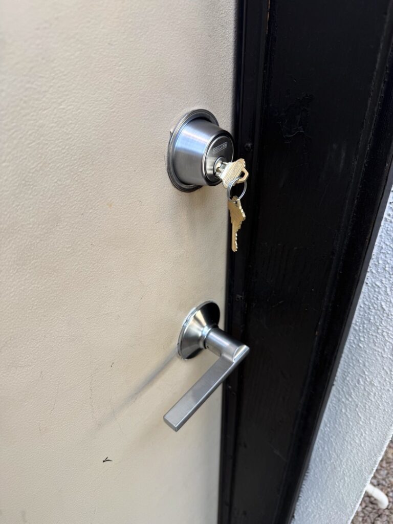 Same-Day Deadbolt Replacement: When to Skip the Hardware Store Trip A black exterior door featuring a silver deadbolt lock with keys inserted and a lever-style door handle below it.