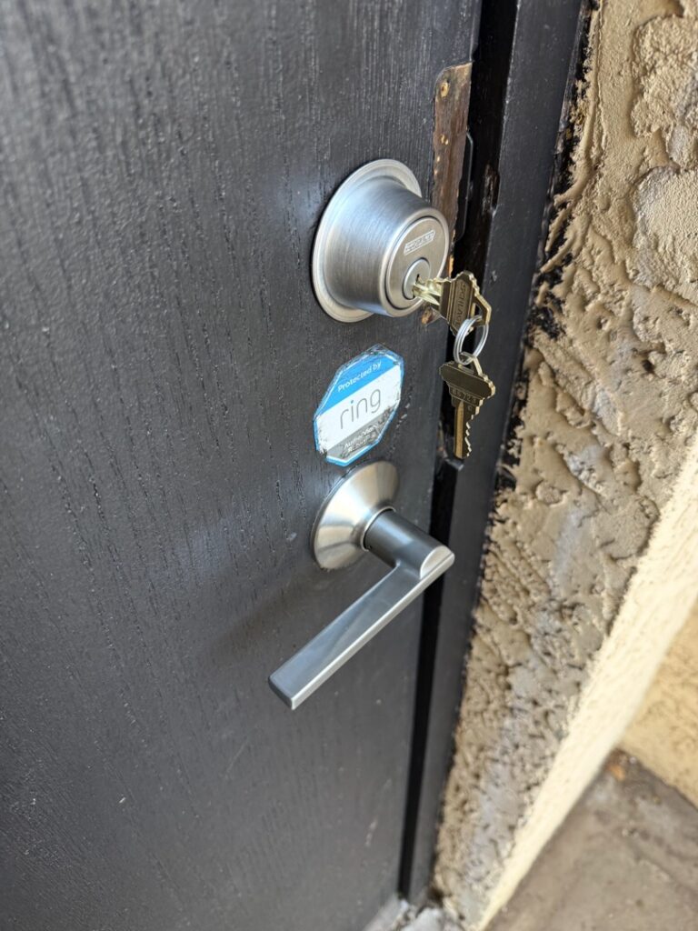 A close-up of a residential door showing a silver deadbolt lock with a key inserted and a lever-style door handle on a dark metal door.