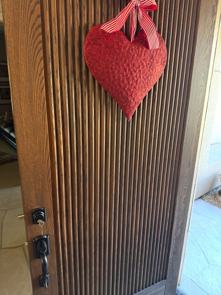 What Makes a Lock 'High Security' — and Is It Worth the Extra Cost? A wood-paneled front door with a black door handle and lock, decorated with a hanging red fabric heart ornament tied with a red ribbon.