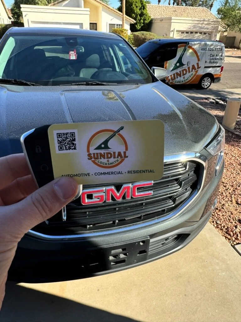 Can You Drive with a Bad Ignition Cylinder — or Is That a Bad Idea? A hand holding a Sundial Locksmith business card in front of a silver GMC truck in a residential driveway with a Sundial service van visible in the background.