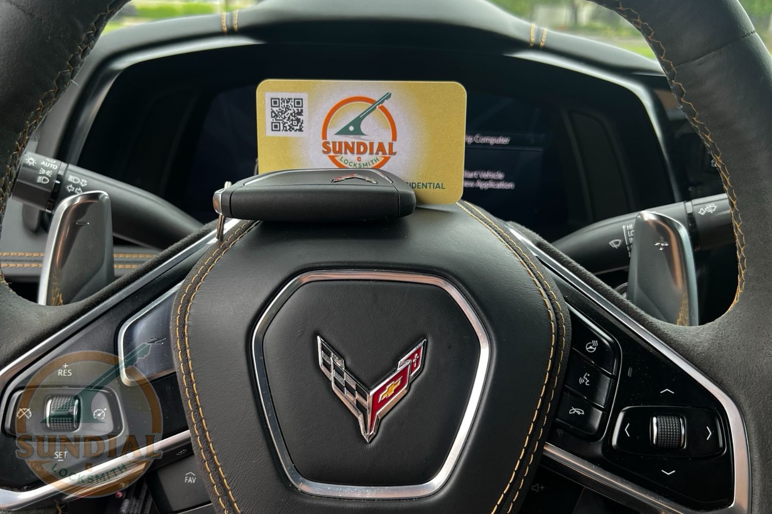 How to Get the Key Code for Your Car — and What a Locksmith Does with It A Sundial Locksmith business card with QR code displayed on the steering wheel of a Chevrolet Corvette with a visible crossed-flags emblem.