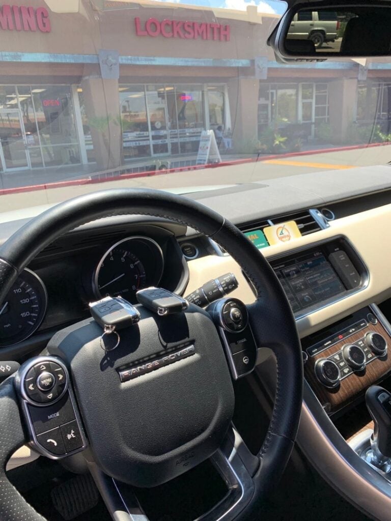 View from inside a Land Rover SUV dashboard looking through the windshield at a locksmith storefront in a strip mall.