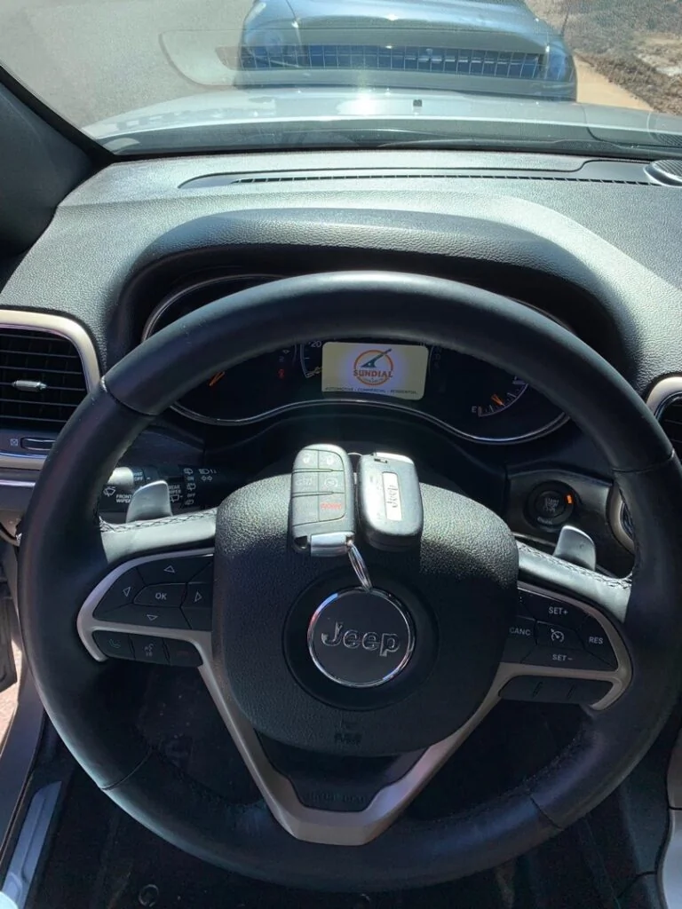 Signs Your Ignition Cylinder Is Failing Before It Strands You Close-up view of a Jeep steering wheel with a key inserted in the ignition switch and multifunction controls visible on the dashboard interior.