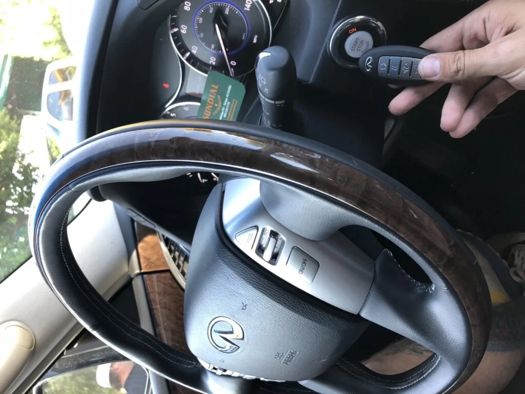 A hand holding a black key fob next to the steering wheel and ignition of a Lexus vehicle during a locksmith programming service.