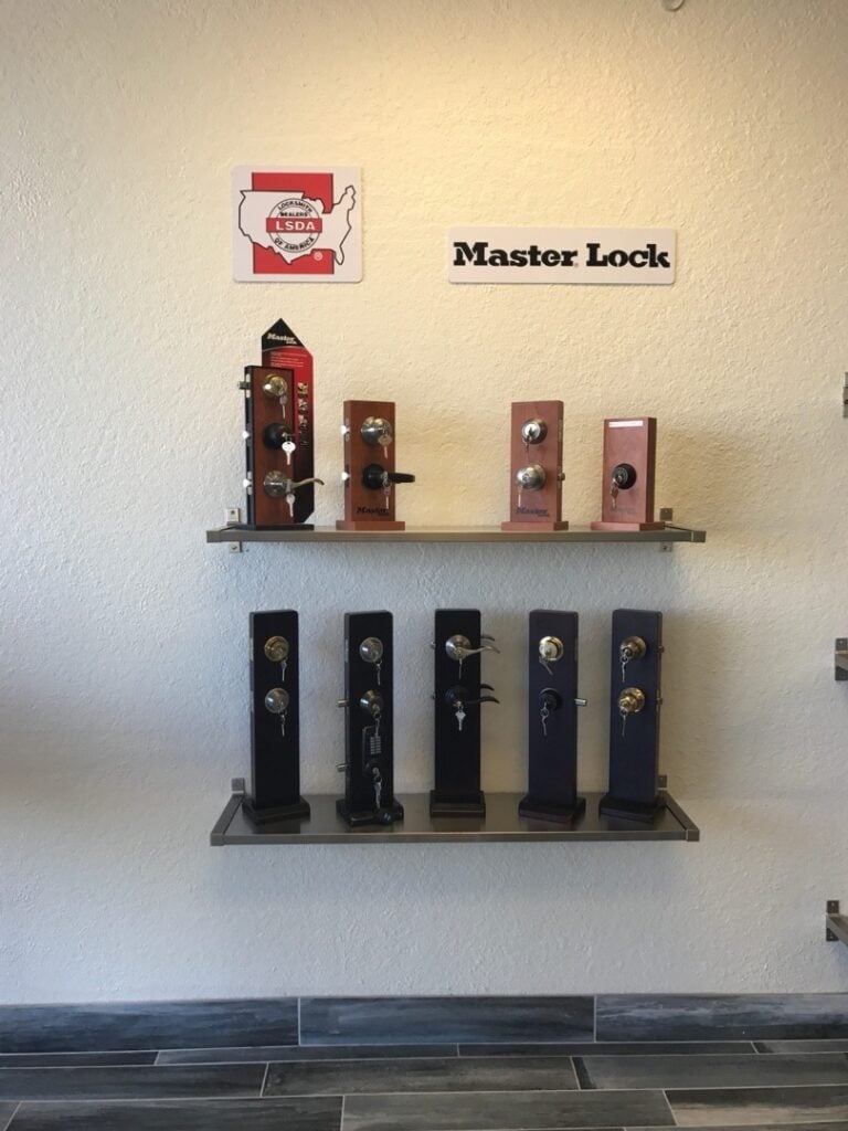 Two wall-mounted metal shelves displaying a variety of Master Lock door locks and deadbolts in a locksmith showroom.