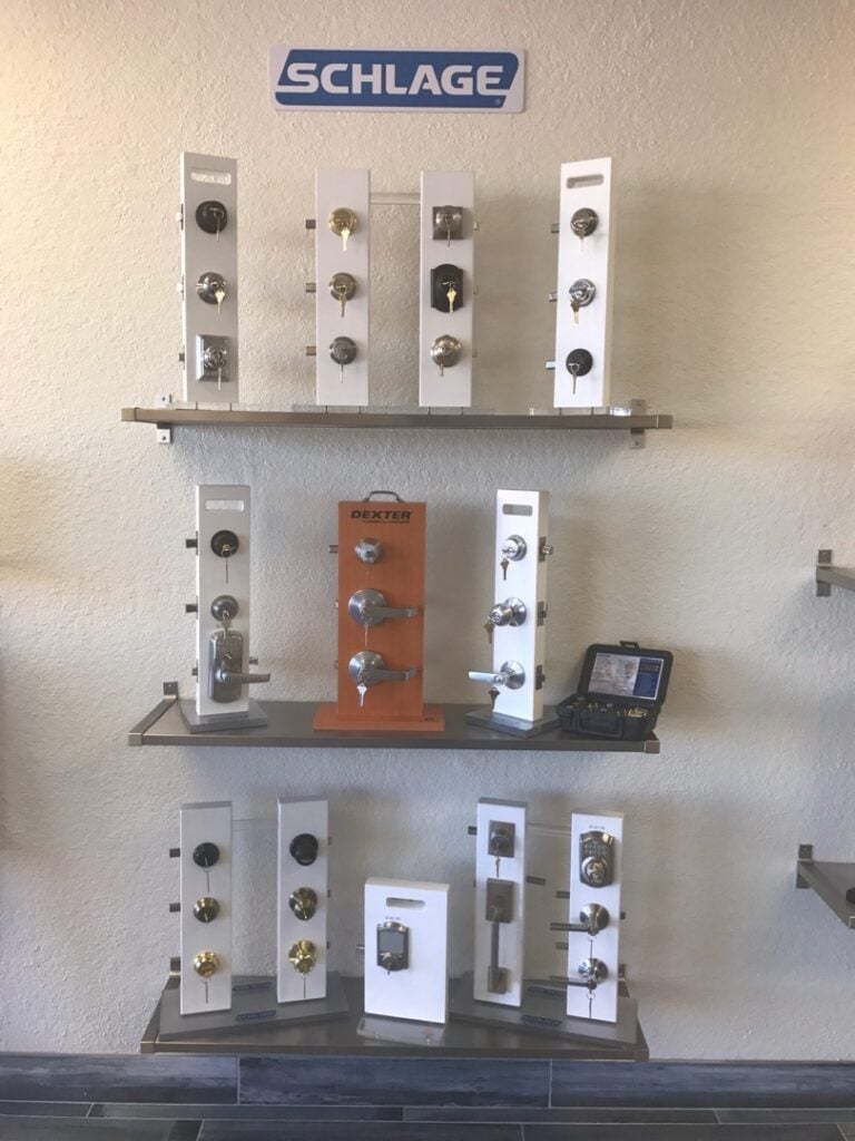 A retail display of Schlage door locks and hardware mounted on three white shelves against a wall, showing various knob, lever, and deadbolt styles.